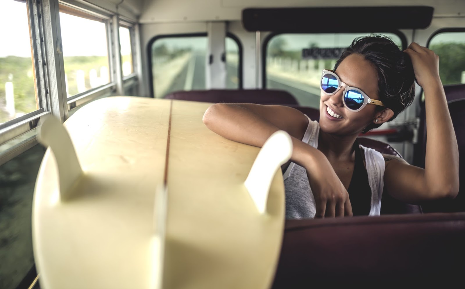 young woman sitting on a bus with a surfboard