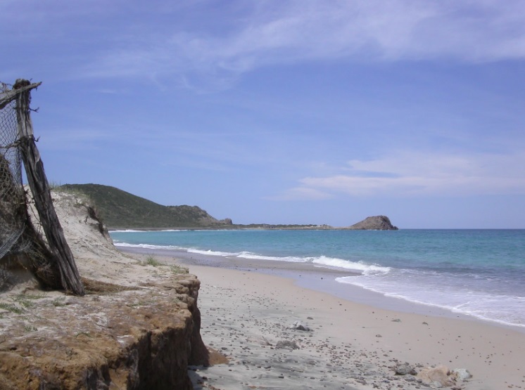 Cabo Pulmo - a beach with a rocky raised area near the left foreground overlooking the sea. There is a rocky island in the distance.