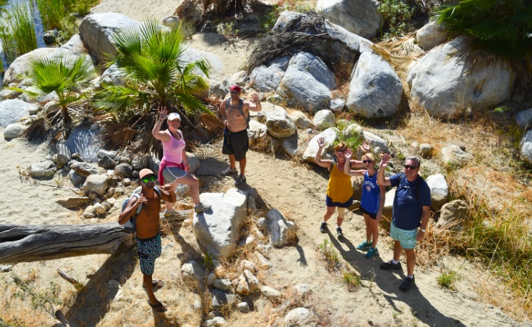 Hiking in Todos Santos and Sierra de la Laguna . A group of 6 people gesture smilingly to the camera among rocks and a tree.